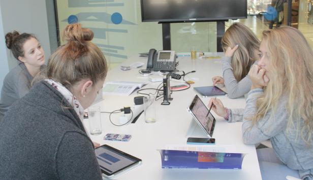 Mehrere junge Frauen sitzen an einem Tisch und arbeiten mit Tablets.