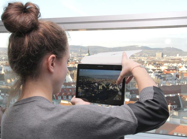 Eine Frau fotografiert mit einem Tablet die Wiener Skyline.