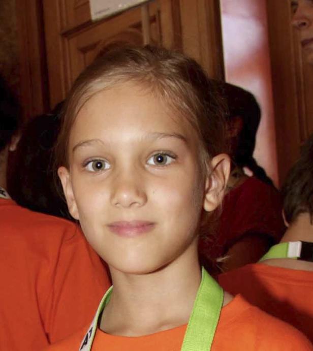 Ein junges Mädchen mit hellbraunen Haaren und grünen Augen lächelt in die Kamera.