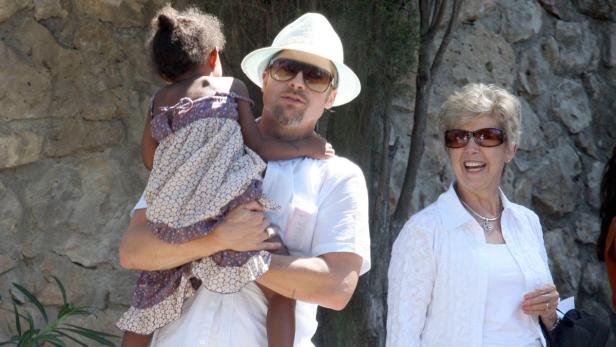 Ein Mann mit Hut und Sonnenbrille hält ein kleines Mädchen im Arm, während eine Frau lächelt.