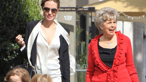 Angelina Jolie mit Sonnenbrille und eine ältere Frau in einem roten Blazer gehen die Straße entlang.