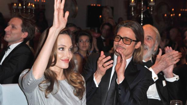 Angelina Jolie hebt die Hand, während Brad Pitt und andere applaudieren.