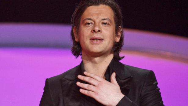 Matthias Schweighöfer in einem schwarzen Anzug vor einem violetten Hintergrund.