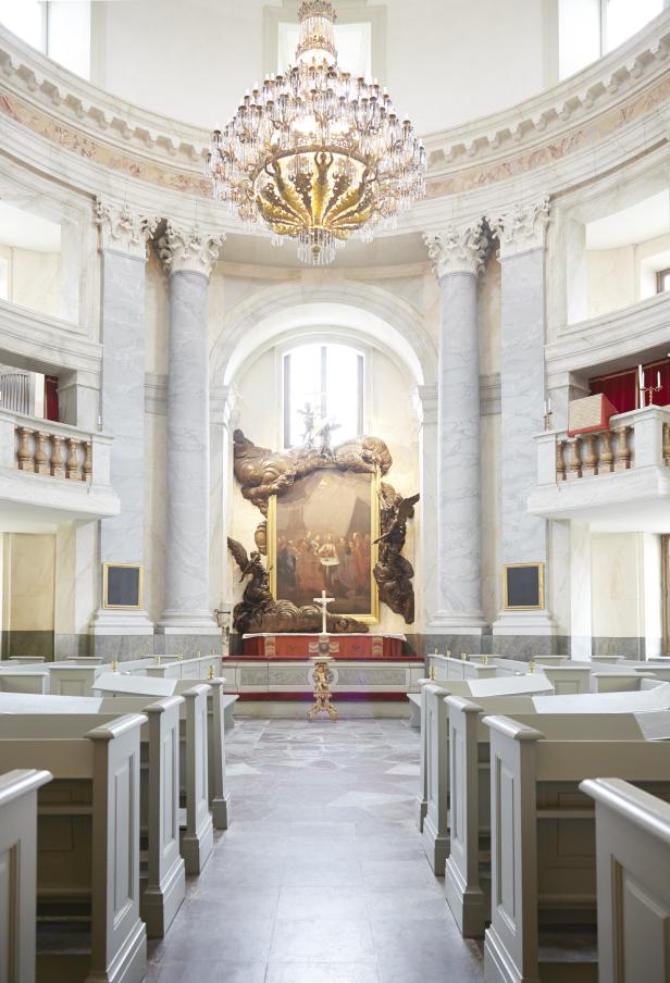 Innenansicht einer Kirche mit Bänken, Säulen und einem Gemälde des letzten Abendmahls.
