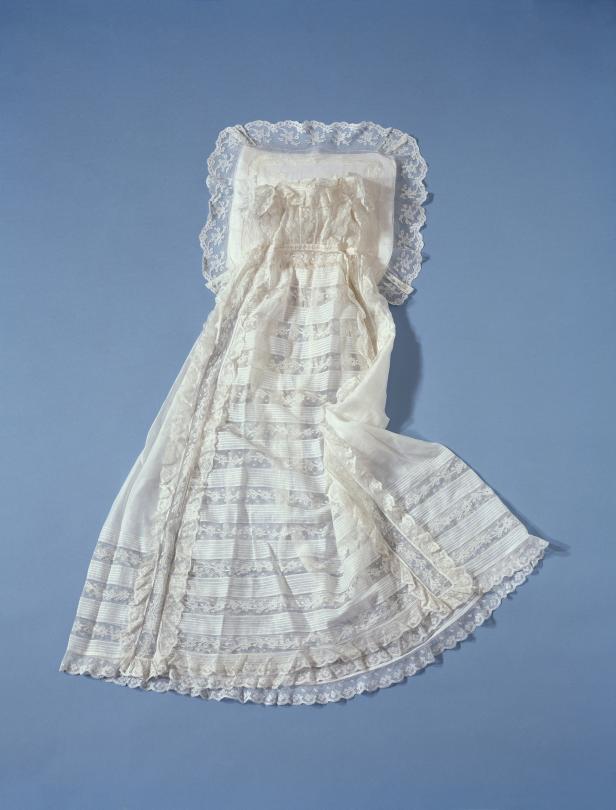 Ein weißes Taufkleid mit Spitze liegt auf einem blauen Hintergrund.