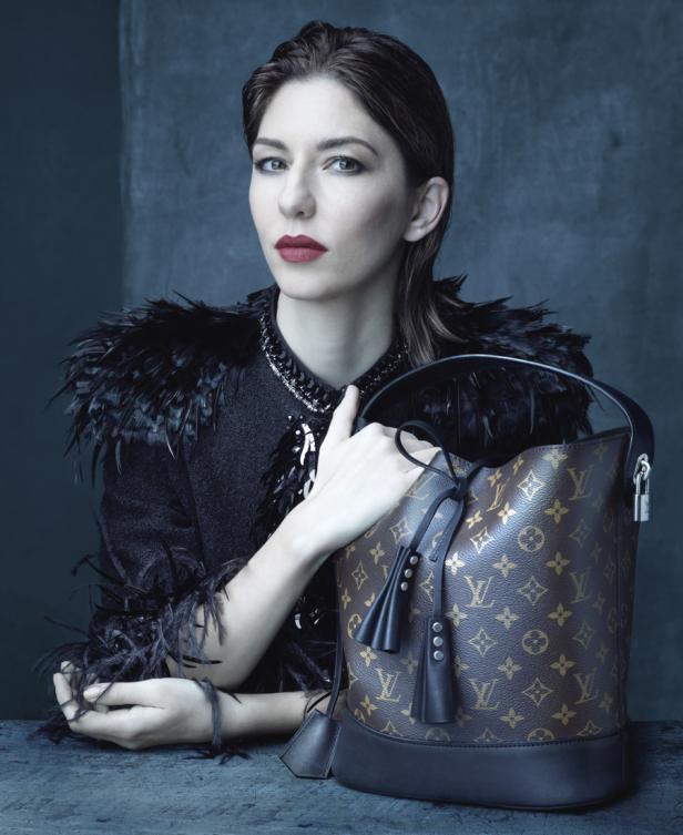 Eine Frau mit dunklem Haar und rotem Lippenstift posiert mit einer Louis Vuitton Handtasche.