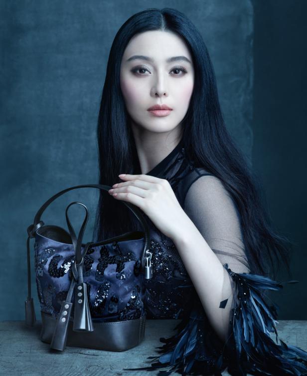 Fan Bingbing posiert mit einer verzierten Handtasche in einem eleganten, dunklen Kleid.