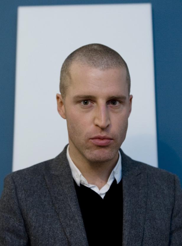 Ein Mann mit kurz geschorenen Haaren trägt ein graues Jackett.