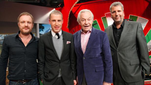 Vier Männer posieren vor einem roten Hintergrund für ein Foto.