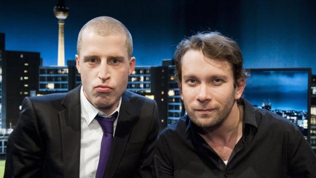 Zwei Männer posieren vor einer Berliner Stadtsilhouette mit dem Fernsehturm.