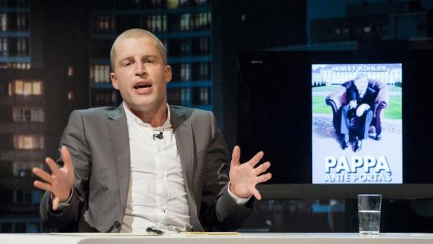 Ein Mann gestikuliert vor einem Bildschirm mit dem Buchcover „Pappa Ante Portas“ von Horst Köhler.