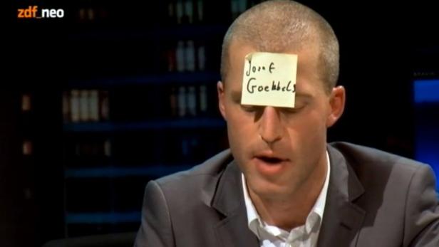 Ein Mann mit einem Zettel mit der Aufschrift „Josef Goebbels“ auf der Stirn.