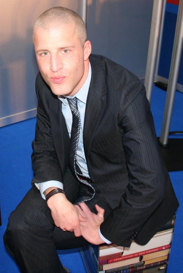 Ein Mann im Anzug sitzt auf einem Stapel Bücher.