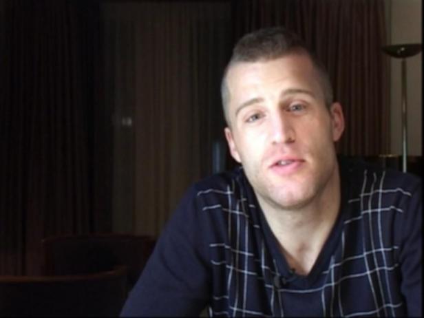 Ein Mann mit kurzen blonden Haaren und einem karierten Pullover schaut in die Kamera.