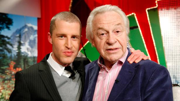 Zwei Männer posieren vor einem farbenfrohen Hintergrund für ein Foto.