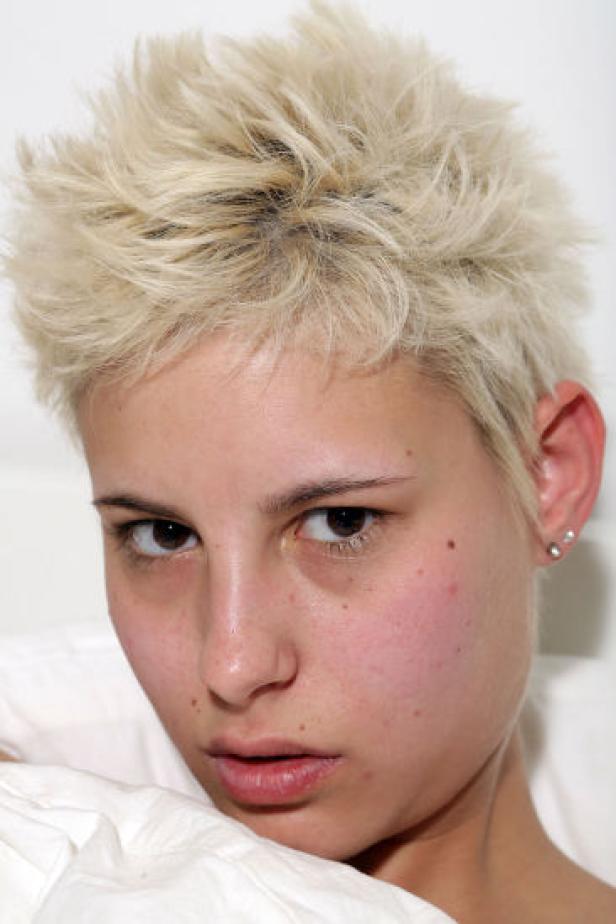 Eine junge Frau mit blonden, kurzen Haaren blickt in die Kamera.