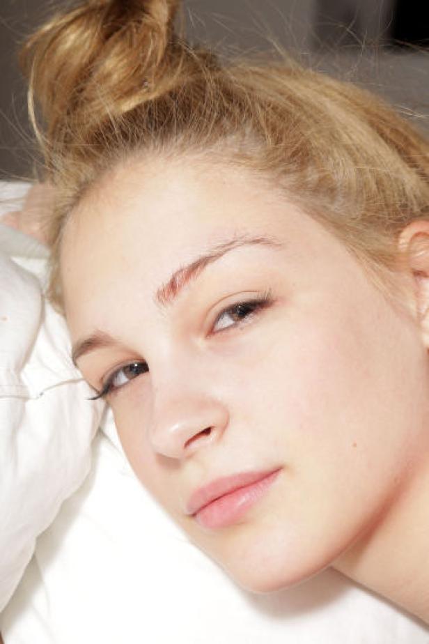 Eine junge Frau mit blonden Haaren liegt auf einem weißen Kissen.