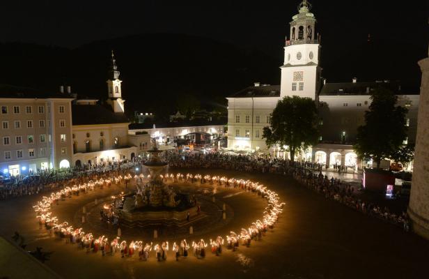 Eine Lichterprozession umrundet einen Brunnen auf einem Platz in Salzburg bei Nacht.