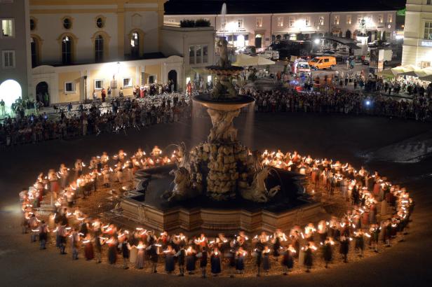 In Salzburg tanzen Menschen mit Fackeln um den Residenzbrunnen.