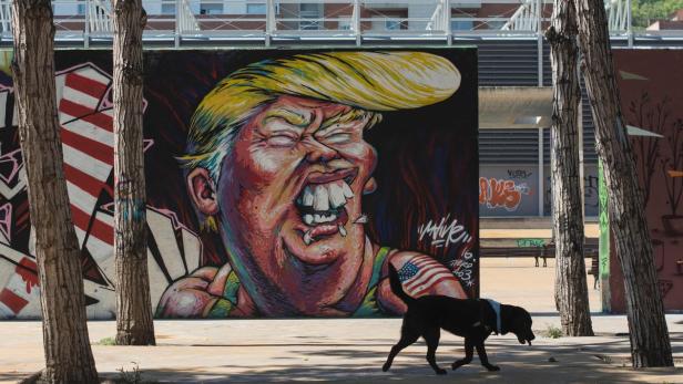 SPAIN-GRAFFITI-FEATURE-TRUMP-USA-STREETART-VOTE Ein Graffiti von Donald Trump mit einer Zigarette im Mund, vor dem ein schwarzer Hund läuft.