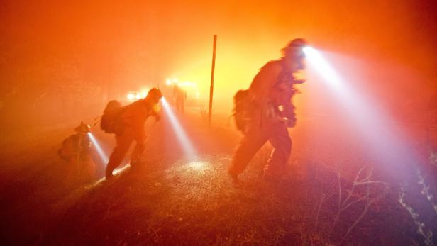 Mehrere Feuerwehrleute gehen mit Stirnlampen durch dichten Rauch.