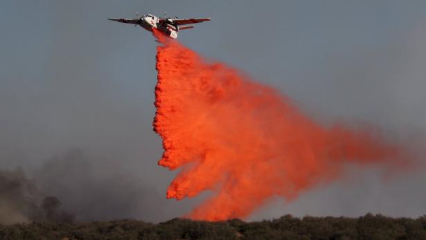Ein Löschflugzeug wirft eine Ladung rotes Löschmittel ab.