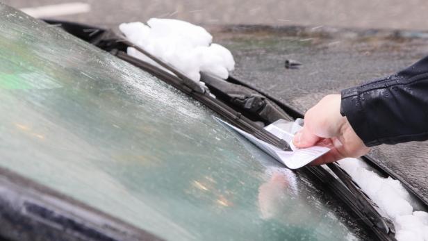 Eine Person befestigt einen neuen Scheibenwischer an einem Auto im Schnee.