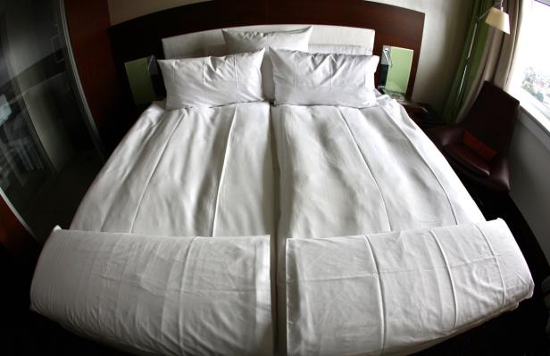 Ein Doppelbett mit weißer Bettwäsche in einem Hotelzimmer.