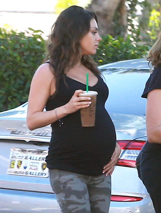 Eine schwangere Mila Kunis mit einem Eiskaffee in der Hand.