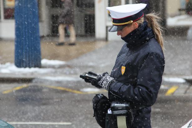 Eine Polizistin in Wien tippt im Schneefall auf einem Gerät herum.