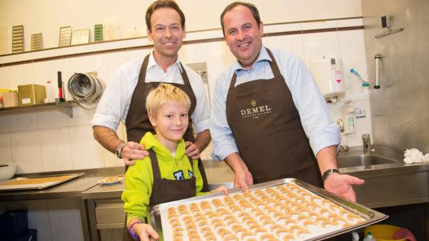 Zwei Männer und ein Kind präsentieren ein Backblech mit Vanillekipferln in einer Konditorei.