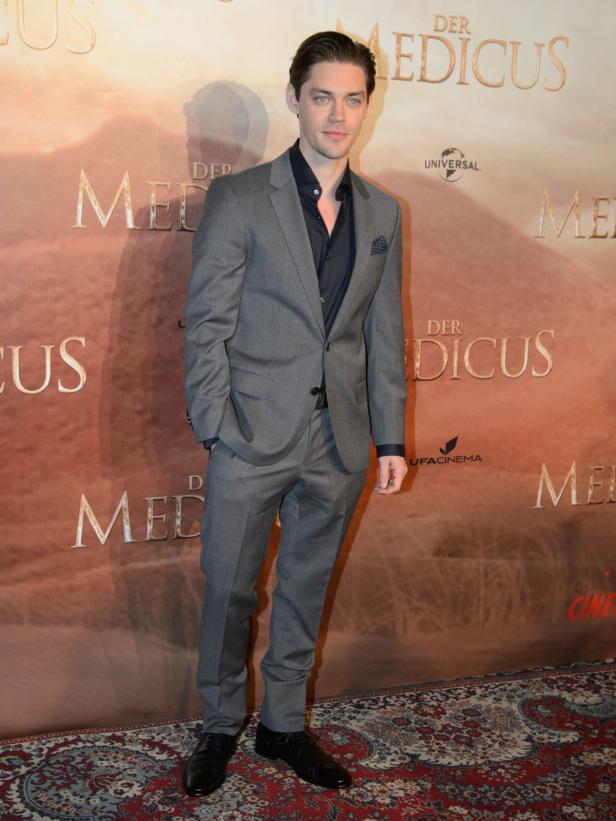 Tom Payne posiert vor einem Poster für den Film „Der Medicus“.