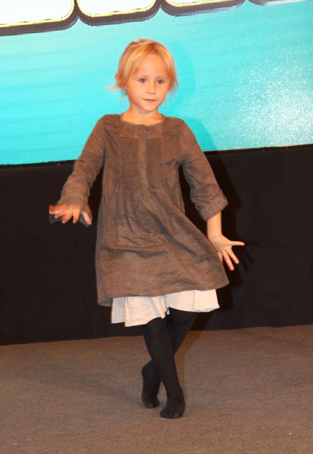 Ein junges Mädchen mit blonden Haaren tanzt auf einer Bühne.