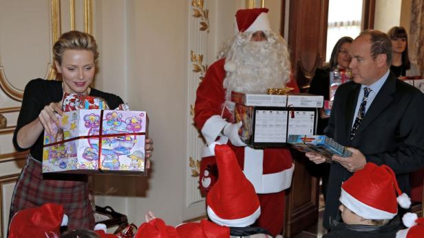 Charlène und Albert von Monaco verteilen Weihnachtsgeschenke, während ein Weihnachtsmann im Hintergrund steht.