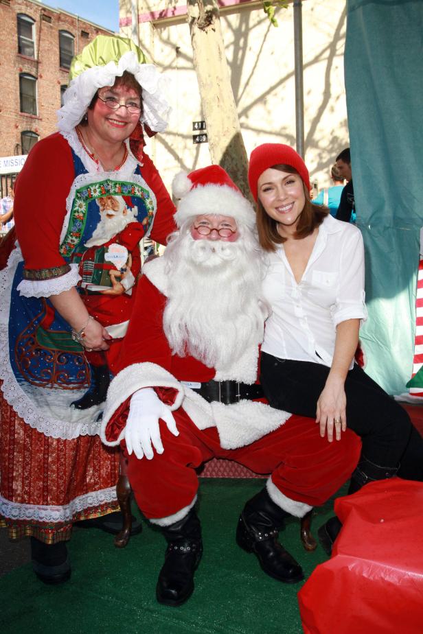Eine Frau sitzt auf dem Schoß eines als Weihnachtsmann verkleideten Mannes, neben einer als Weihnachtsfrau verkleideten Person.