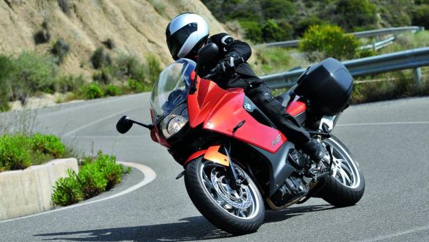 Ein Motorradfahrer fährt mit einer roten BMW F800 GT auf einer kurvenreichen Straße.