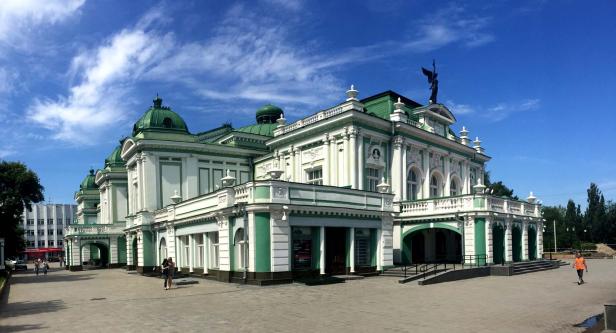 Das Staatliche Akademische Opern- und Balletttheater Nowosibirsk mit grünen Kuppeln unter blauem Himmel.