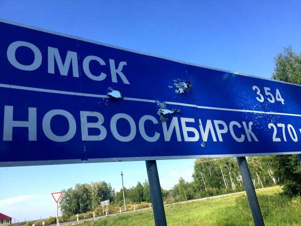 Ein blaues Schild mit den Aufschriften Omsk und Nowosibirsk, das Einschusslöcher aufweist.