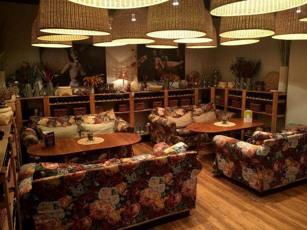 Ein gemütlicher Raum mit floralen Sofas, Holztischen und rustikalen Regalen unter großen Lampen.