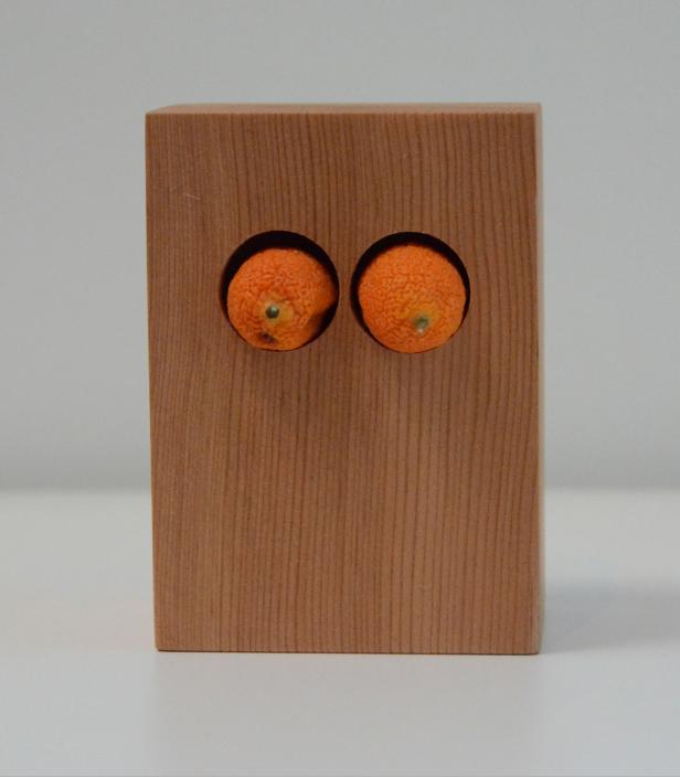 Ein Holzblock mit zwei Mandarinen, die wie Augen in runden Löchern stecken.