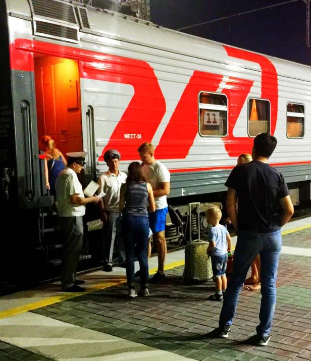 Reisende steigen in einen russischen Zug ein, während ein Schaffner die Tickets kontrolliert.