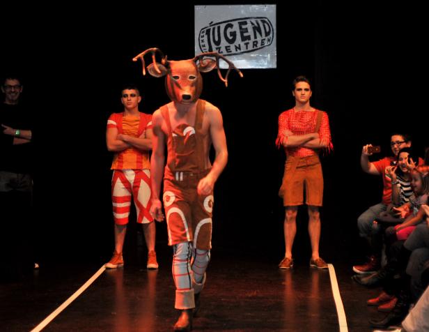 Ein Mann mit einer Hirschmaske läuft auf einem Laufsteg vor Zuschauern.