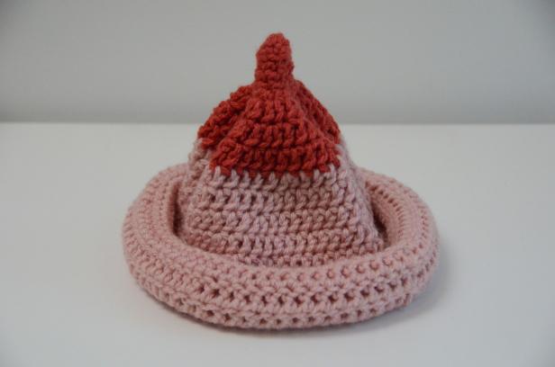 Ein gehäkelter Hut in Rosa und Rot liegt auf einem Tisch.