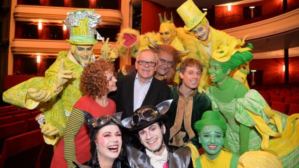 … Eine Gruppe von Darstellern in farbenfrohen Kostümen posiert auf einer Theaterbühne.