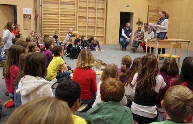 Eine Gruppe von Schulkindern sitzt auf dem Boden und hört einem Vortrag zu.