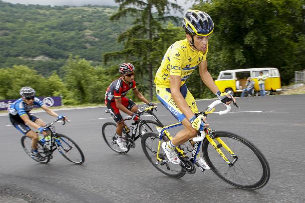 Radrennfahrer in gelbem Trikot führt ein Rennen auf einer asphaltierten Straße an.