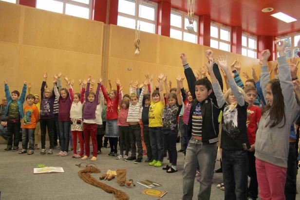 Eine Gruppe von Kindern steht in einem Raum und streckt die Arme in die Höhe.