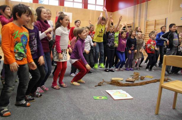 Eine Gruppe Schulkinder steht in einem Raum, einige mit erhobenen Armen, vor einer Karte von Brasilien.