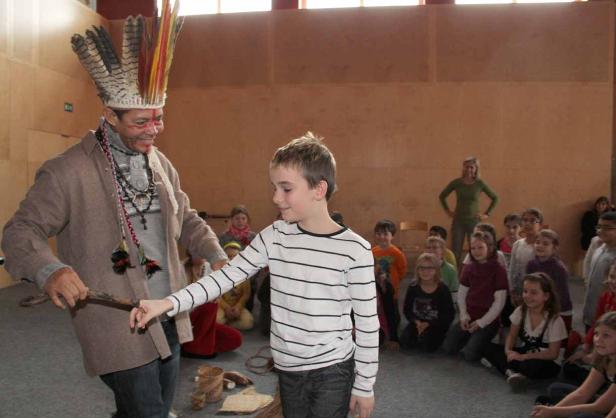 Ein Mann mit Federschmuck interagiert mit einem Jungen vor einer Gruppe von Kindern.