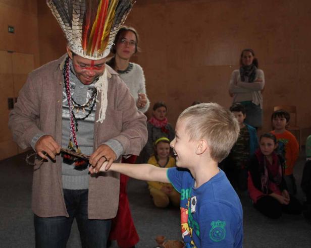 Ein Mann mit Kopfschmuck interagiert mit einem Jungen vor einer Gruppe von Kindern.
